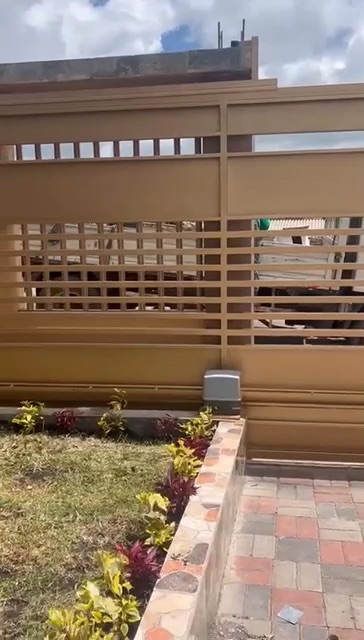 Port&oacute;n corredizo beige de listones desliz&aacute;ndose junto a un jard&iacute;n