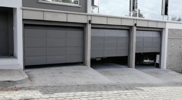 Tres puertas seccionales grises operando en los garajes de un edificio residencial